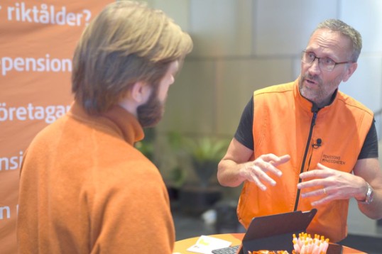 Färgfotografi: Två personer med orange tröjor pratar pension