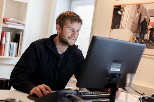 Man i mörk tröja sitter framför datorn och besöker Försäkringskassans webbplats.