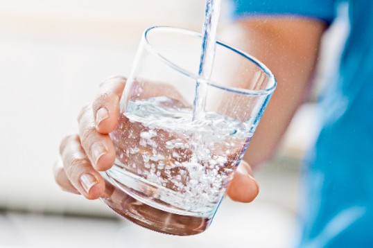 En varm person häller upp ett glas vatten för att svalka sig i sommarvärmen.